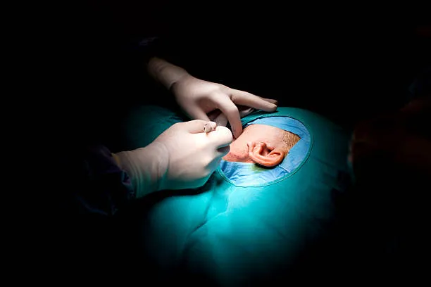 image10 | Head N Neck Surgery Surgeons in sterile gloves operate on a patient’s ear, with a blue sterile drape and focused lighting during surgery.