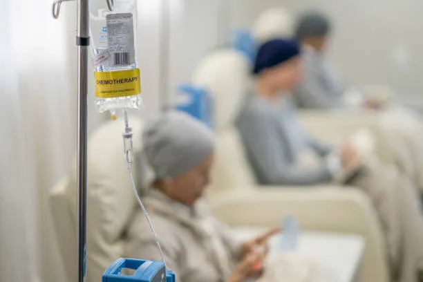 image7 | Head N Neck Surgery IV chemotherapy infusion bag in focus with tubing, while patients receive treatment in recliner chairs in a clinical setting, blurred in the background.
